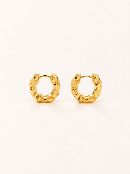 A pair of textured gold huggie hoop earrings on a clean, solid off-white background.