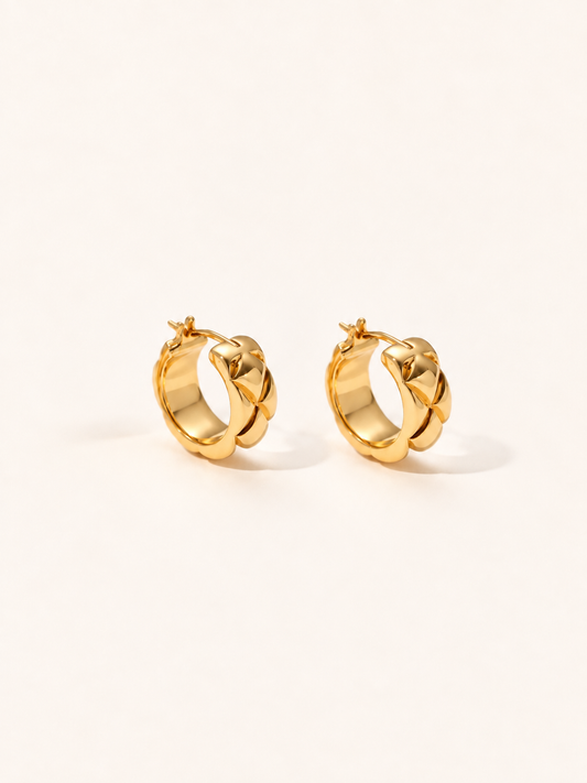 A pair of gold huggie hoop earrings with a textured, ridged outer surface, displayed on a clean off-white background.