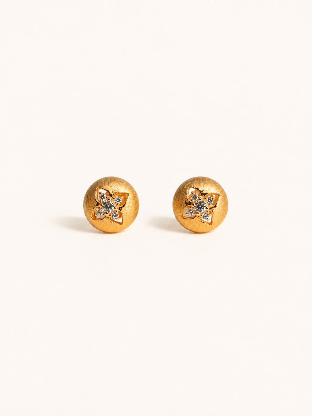 A pair of gold round stud earrings with a small flower-shaped crystal cluster in the center, set against a plain off-white background.