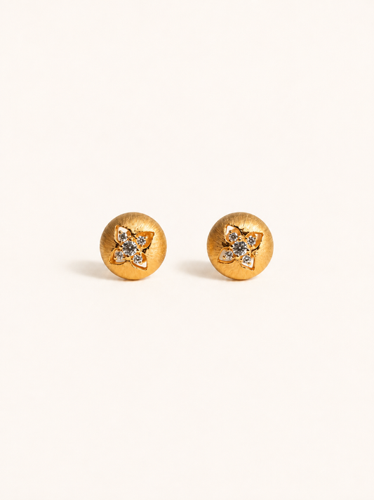 A pair of gold round stud earrings with a small flower-shaped crystal cluster in the center, set against a plain off-white background.