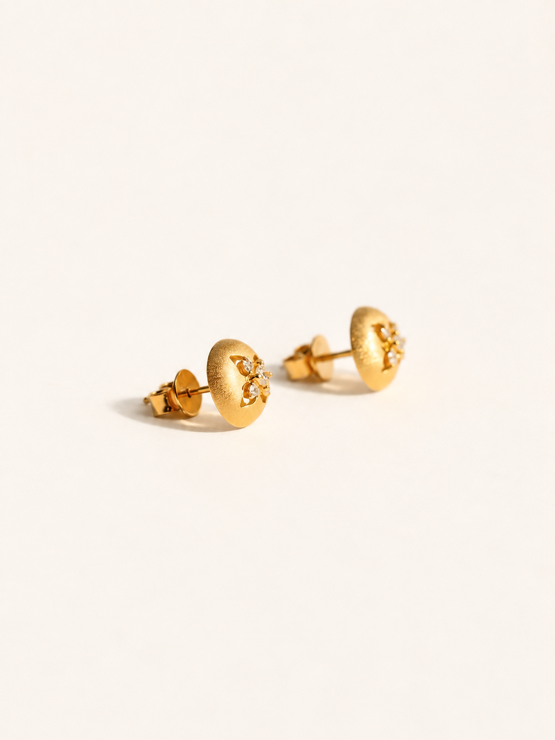 A pair of textured gold stud earrings with small clear crystal accents, displayed on a clean off-white background.