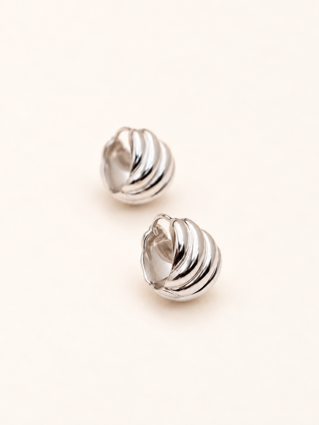A pair of silver-toned twisted hoop earrings with a ribbed, spiral design, displayed on a clean, light cream background.