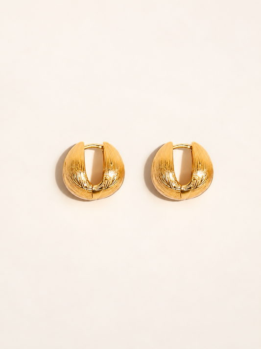 A pair of textured gold huggie hoop earrings on a clean, solid off-white background.