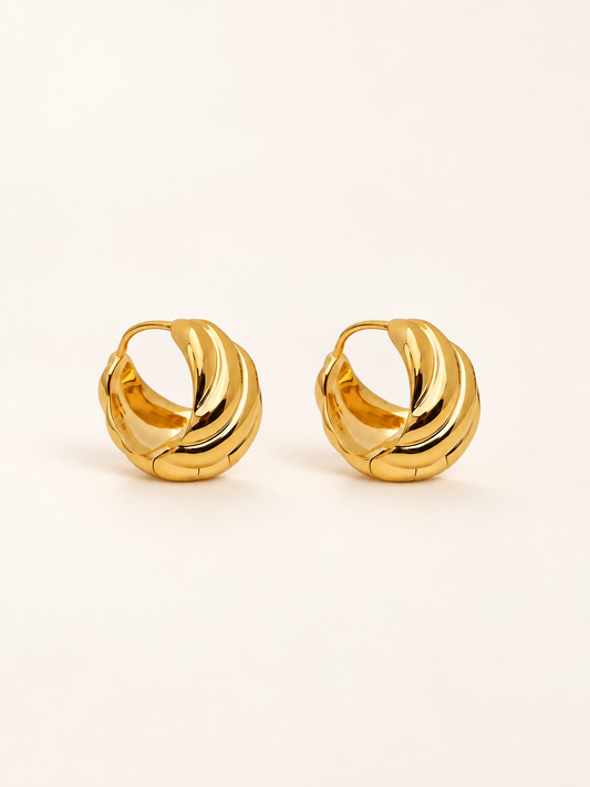 A pair of gold huggie hoop earrings with a twisted, textured design, displayed on a clean off-white background.
