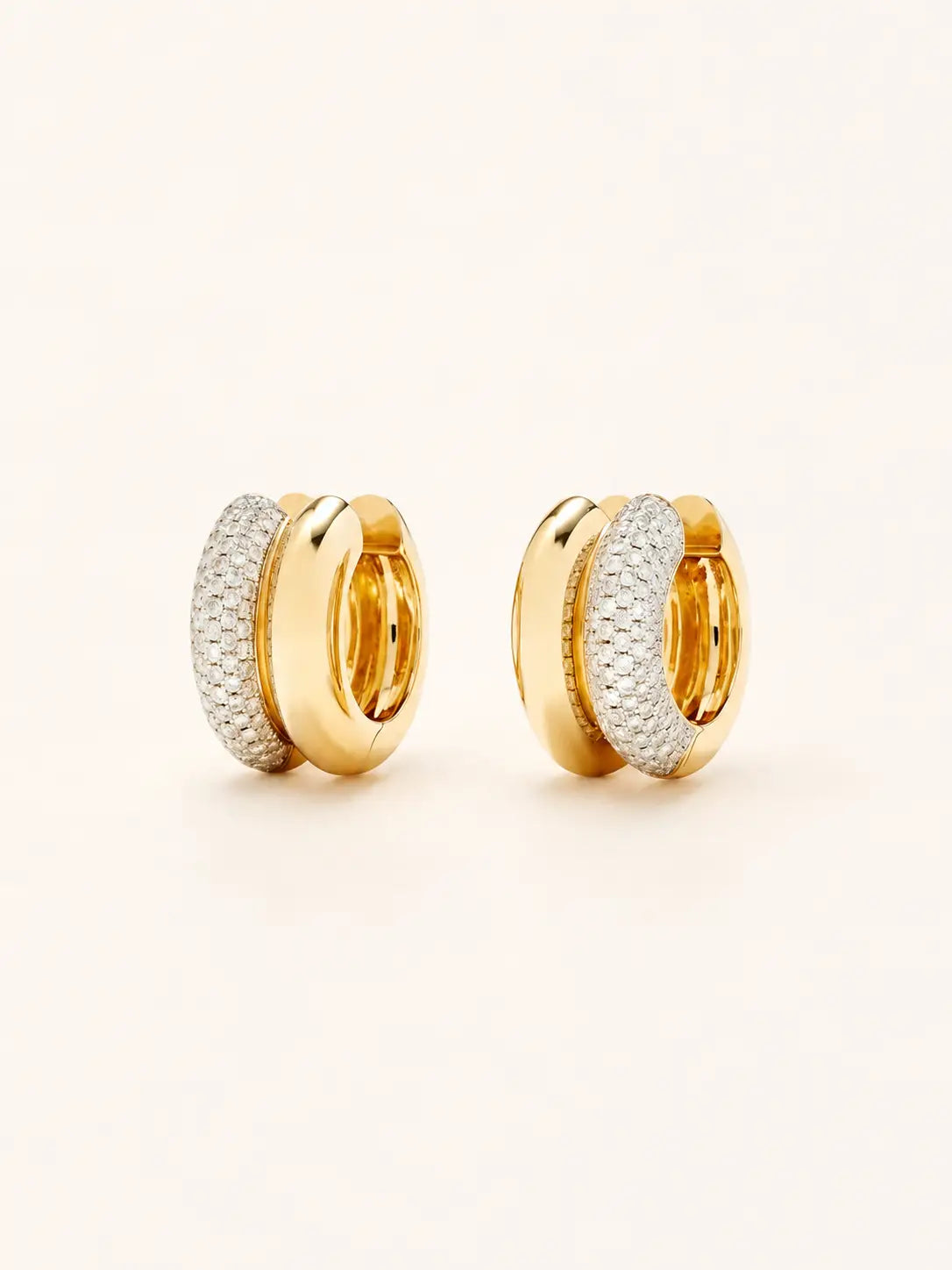 A pair of gold  hoop earrings with textured pavé-set clear stones on the front, photographed on a clean, light cream background.