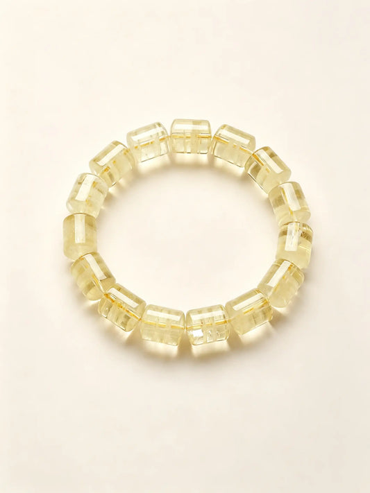 A beaded stretch bracelet made of faceted, translucent pale yellow cube-shaped beads, arranged in a circle on a warm off-white background.